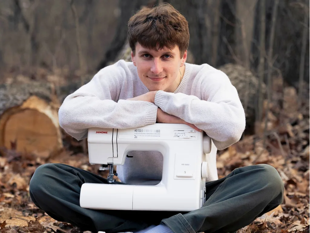 Mason sits outdoors with a white sewing machine in front of him.