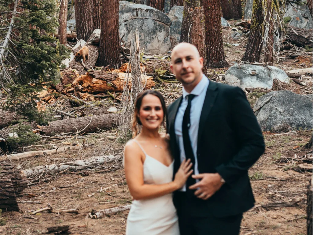 Kelly and Stephen pose during their Yosemite wedding shoot while a bear walks through the forest behind them.