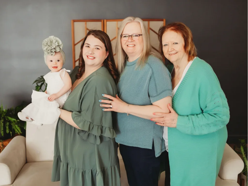Four generations of a family pose together, including a baby, a young woman, an older woman and an elderly woman.