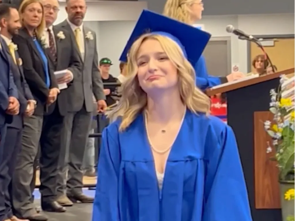 Sydnie stands at her graduation ceremony in a blue cap and gown before her Navy brother Skylar surprises her.