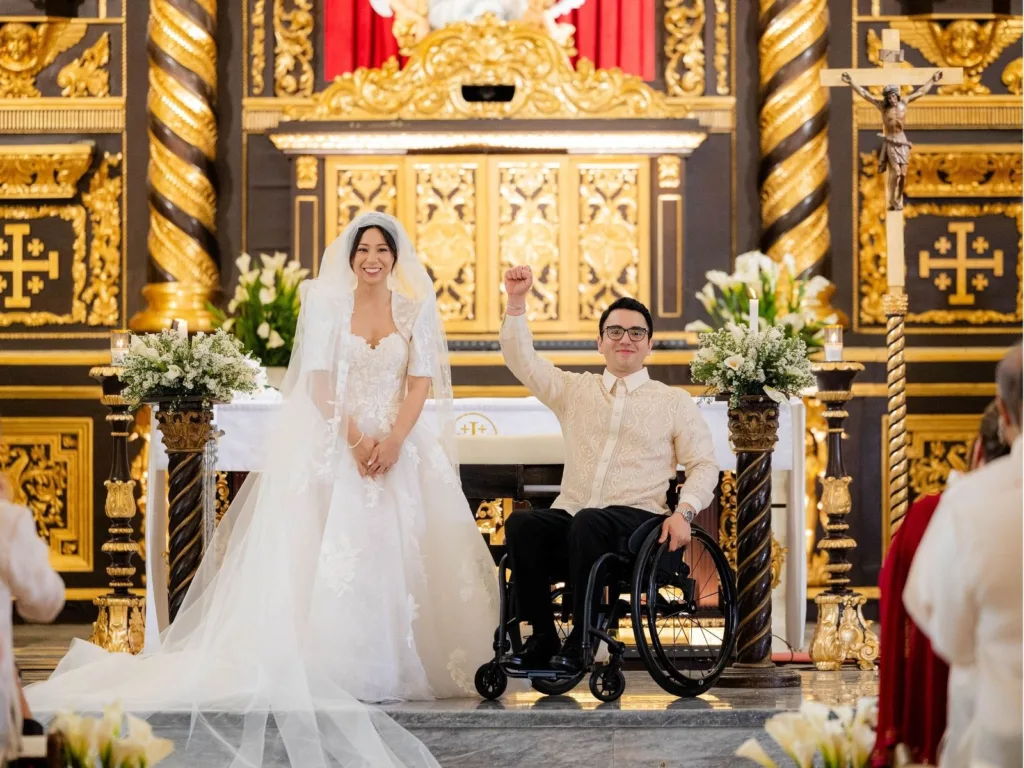 Michelle smiles beside Andy as he sits in his wheelchair at the altar during their church wedding.