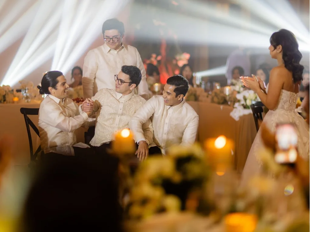 Andy’s groomsmen help support him as he stands in front of Michelle during their wedding reception.